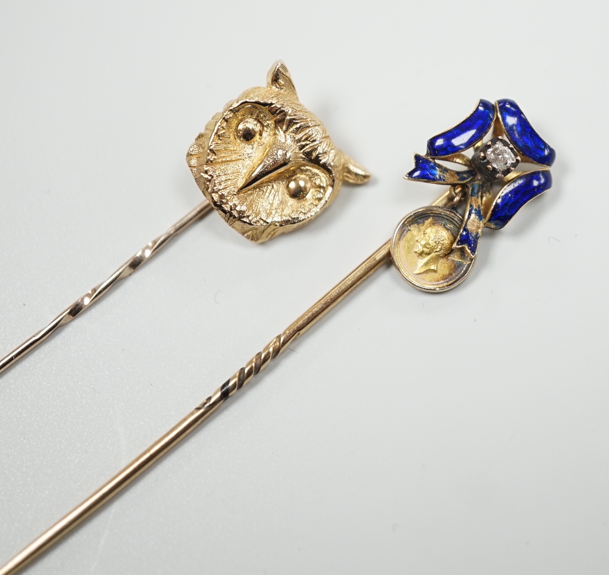 An early 20th century yellow metal enamel and diamond set ribbon bow stick pin, hung with a miniature medallion, 63mm and a later 9ct gold stick pin, gross 5.2 grams.